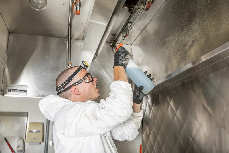 Technician spraying cleaning solution inside an exhaust canopy next to the hood light